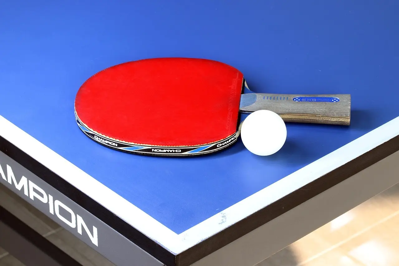 Rødt bordtennisbat og hvid bordtennisbold på blåt bord