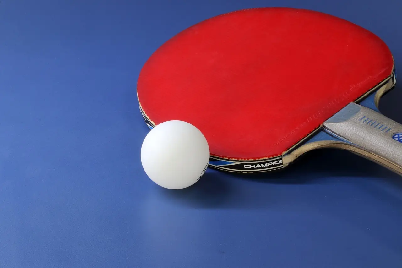 Rødt bordtennisbat og hvid bold på blå baggrund